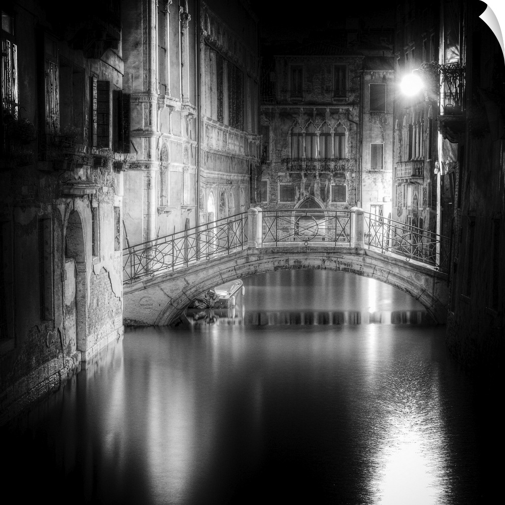 High contrast black and white image of a bridge in a canal in the center of a city at night.