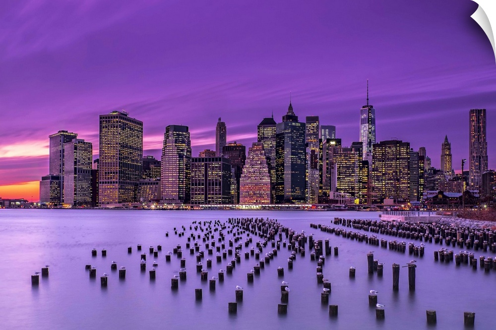 Manhattan skyline at sunset under a purple sky, seen from Brooklyn.