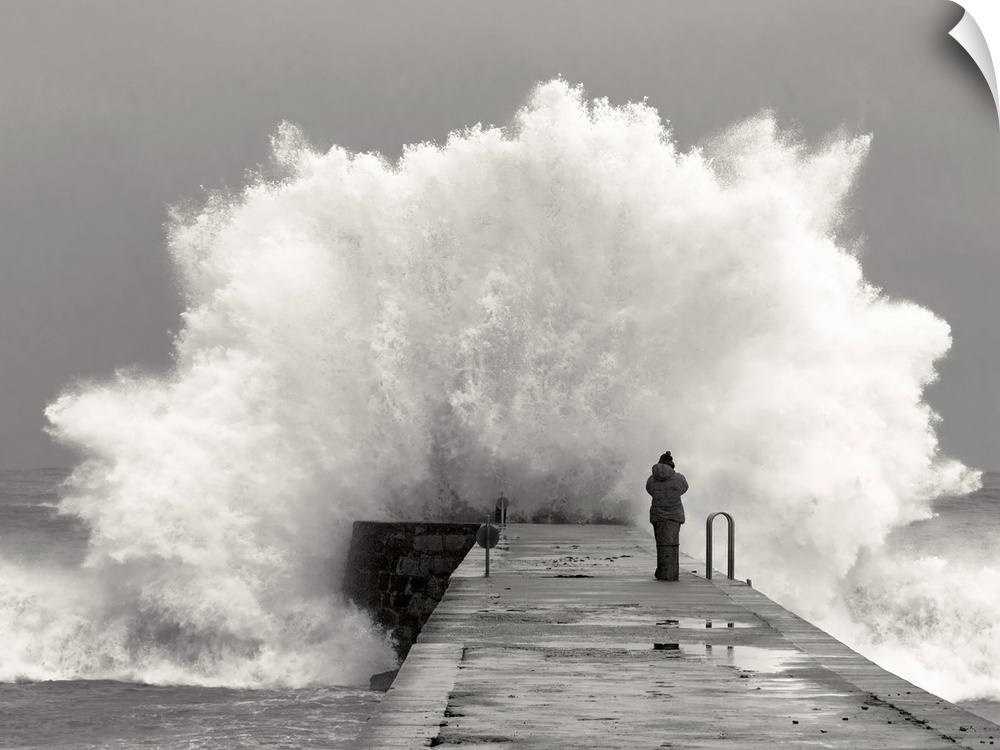 A photographer standing on a pier with waves crashing.