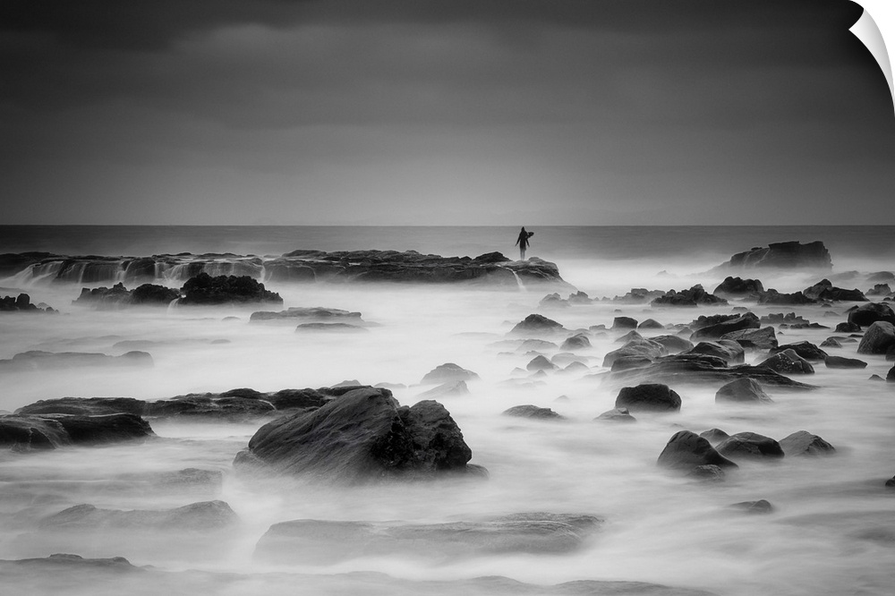 A figure stands in the distance on a rock protruding from the misty ocean.