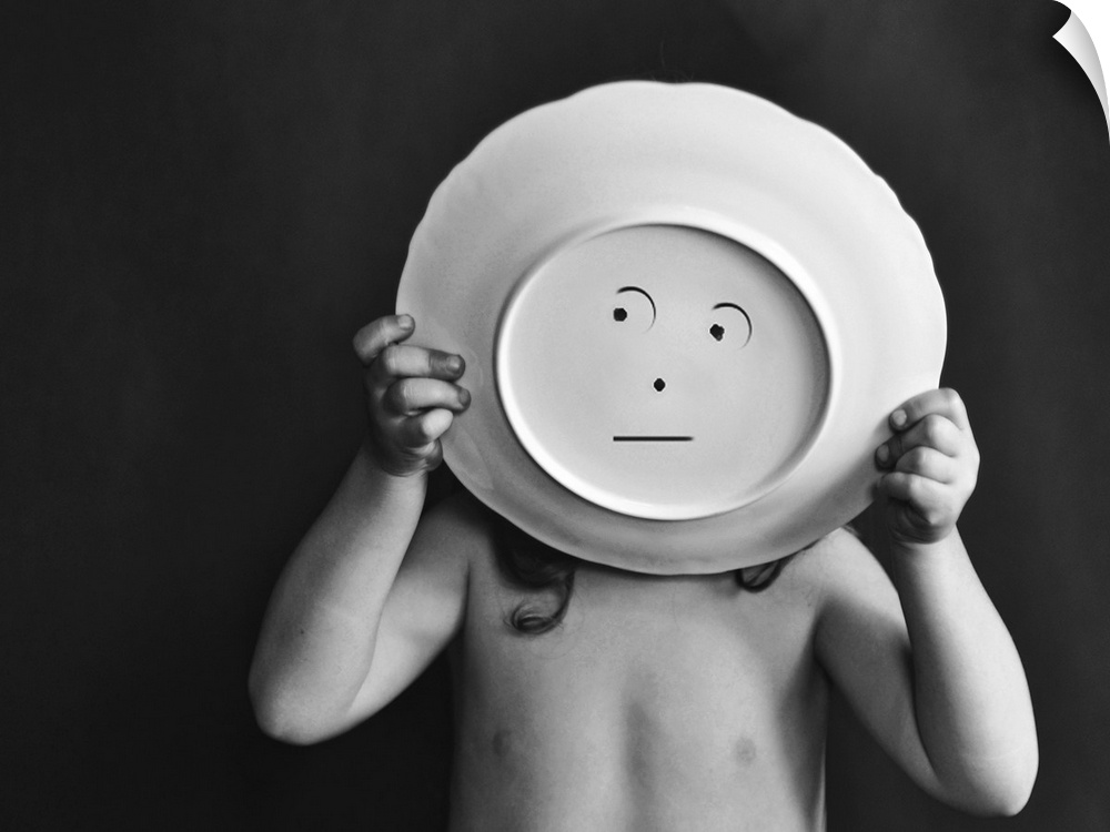 A child holds up a bowl with a simple face drawn on the bottom.