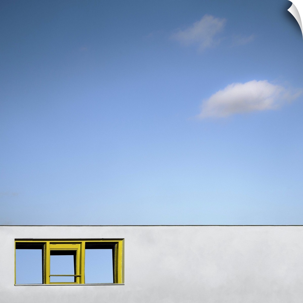 Abstract view of a yellow framed window on a blank white wall facade, under a blue almost cloudless sky.