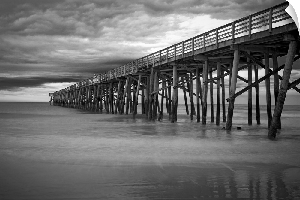 A black and white photograph of a long pier jetting out over the ocean.