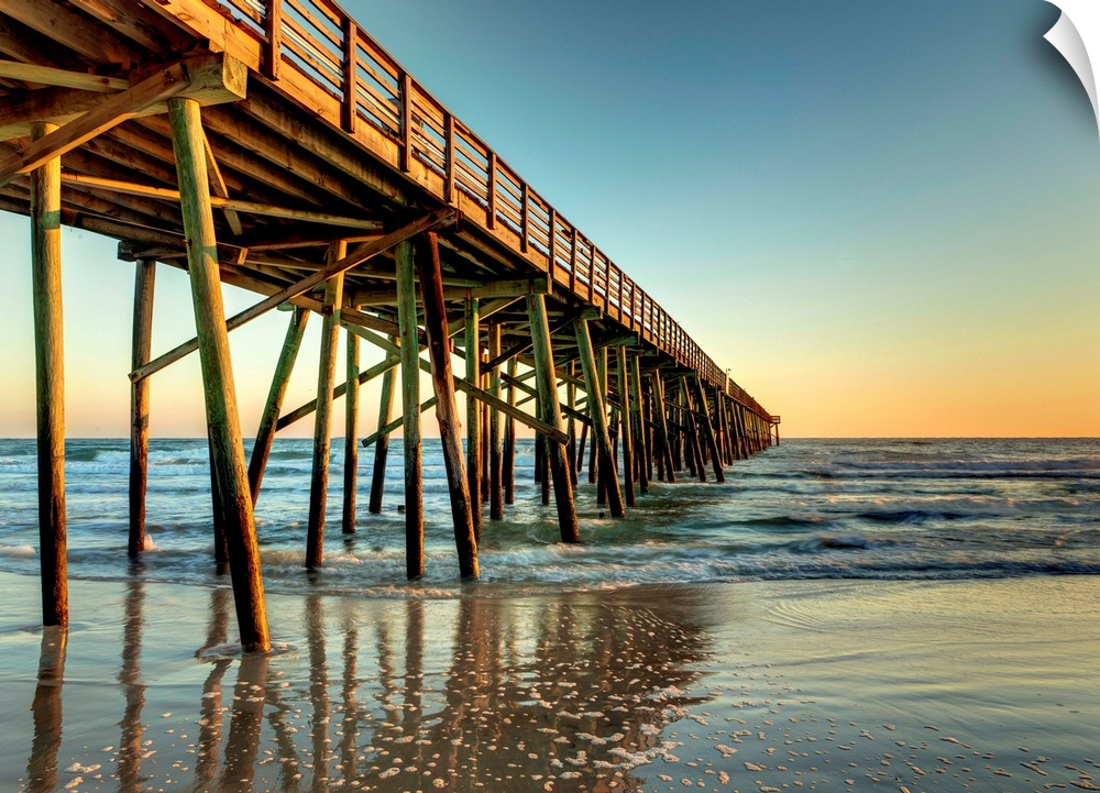 A photograph of a long pier jetting out over the ocean. Sunlight glowing over the horizon as the sun rises.