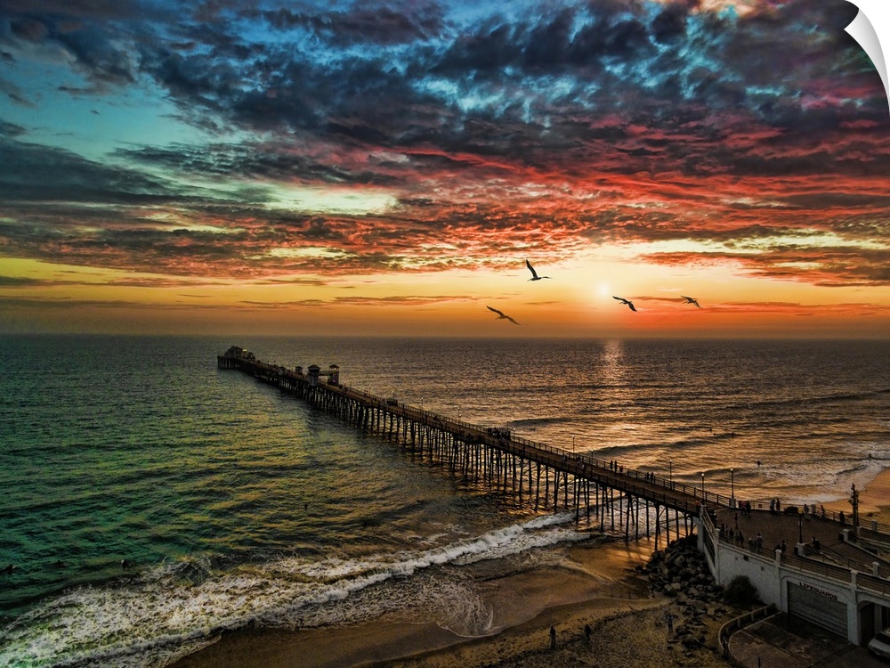 Pelicans glide past a dramatic and colorful sunset near the Oceanside Pier, Oceanside, California, USA. Oceanside is 40 mi...