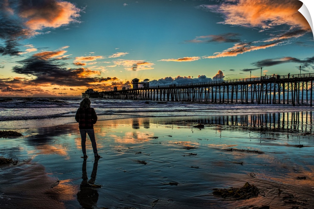 A woman stands in reflective sands near the Oceanside Pier, Oceanside, California, USA.