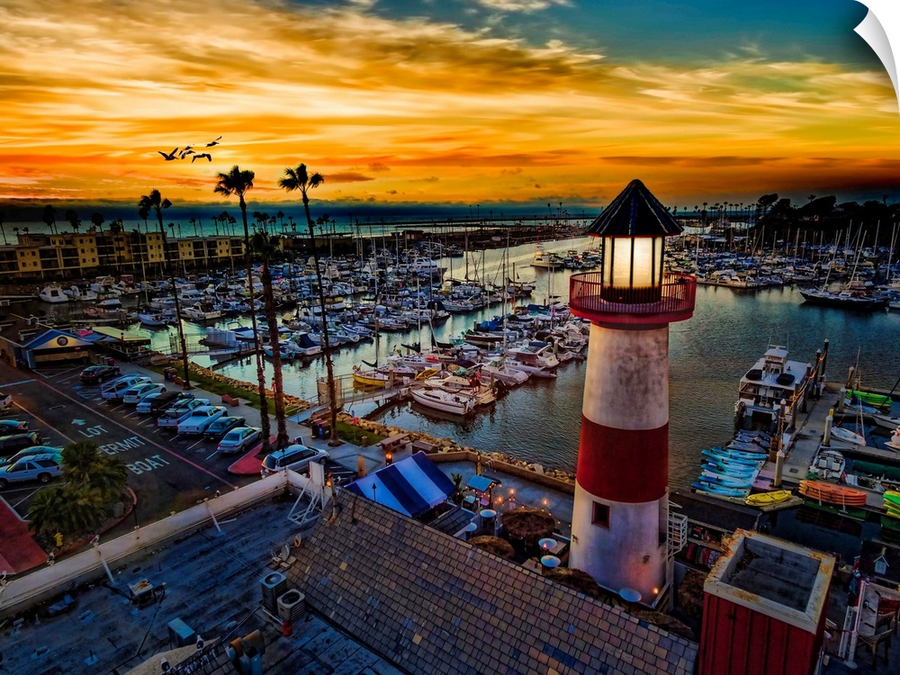 Pelicans glide over the Oceanside Harbor and the little lighthouse glows. Colorful sunset in Oceanside, California, USA.