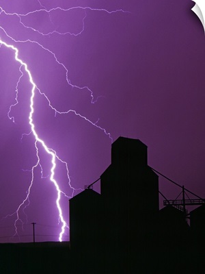 A bolt of lightning lights up the night sky during a storm silhouetting a grain elevator