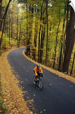 A cyclist rides along a rural road in the fall.; Vermont, USA.