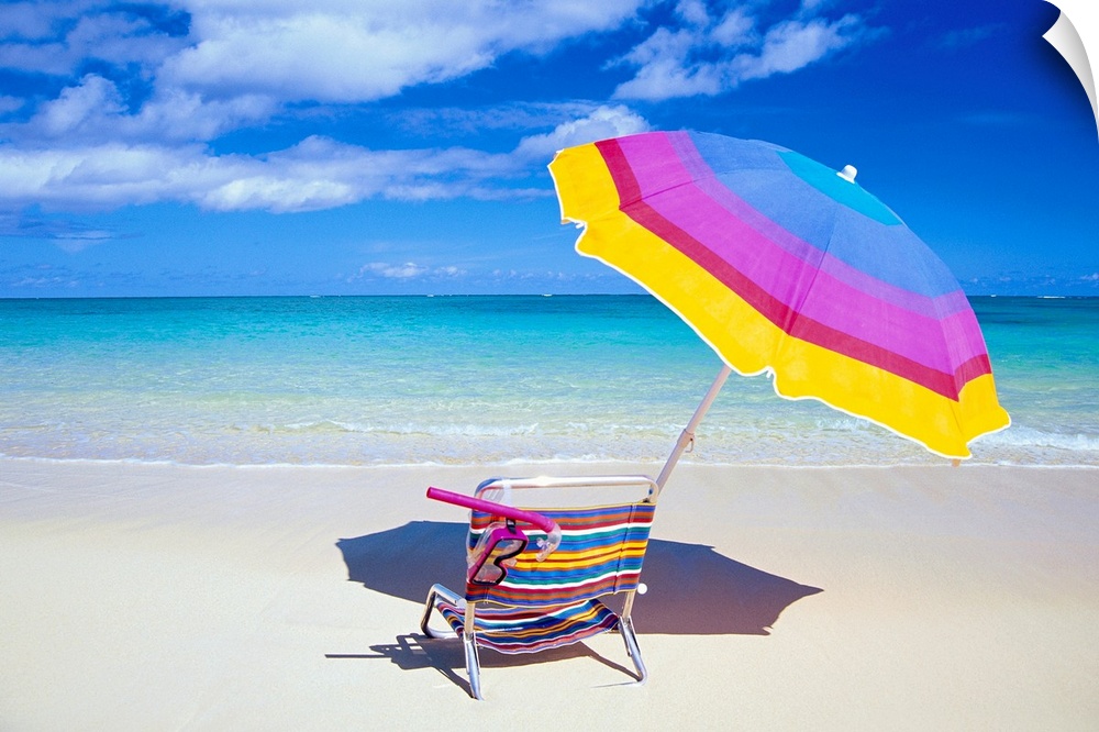 A large photograph of a colorful beach chair and umbrella sitting solely on the sand close to the clear ocean water.