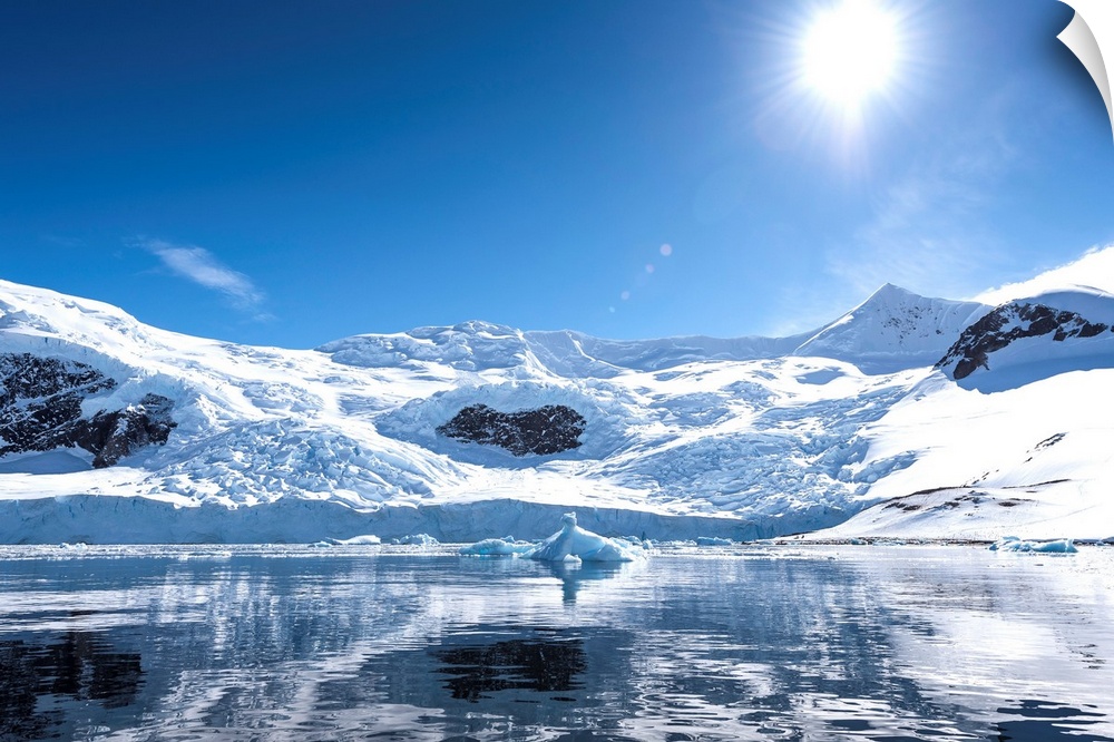 Bright sun and snow on the mountains reflected in the water of Neko Harbor, Antarctica.