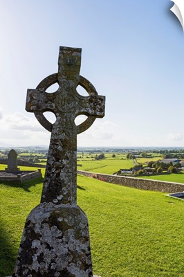 Celtic cross on grassy hill with stone wall under blue sky, Cashel, Ireland