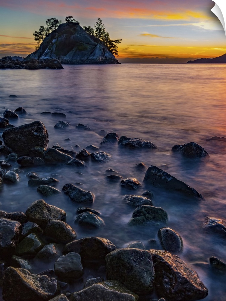 Golden sunlight illuminating the clouds in the distance and wet rocks along the shoreline; Vancouver, British Columbia, Ca...