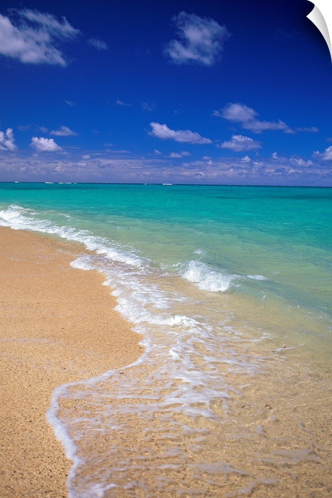 Shallow waters recede from the sandy coastline of a tropical beach, the clear sea stretching out into the distance.