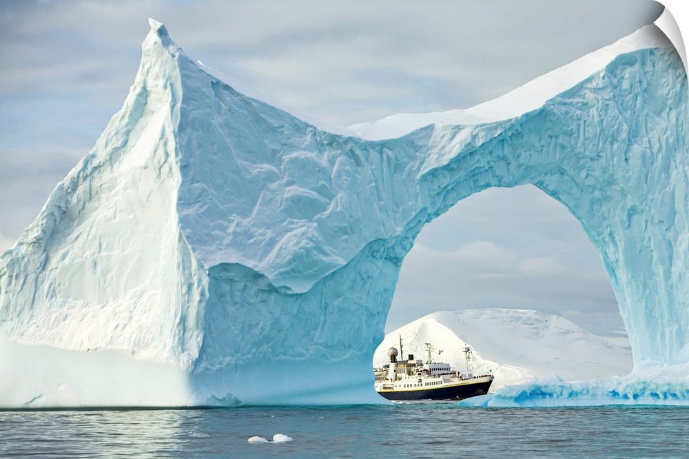 Iceberg with arch frames an expedition ship in the Yalour Islands of Antarctica, Yalour Islands, Antarctica