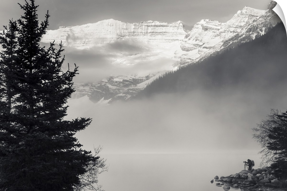 Silhouette of a photographer on the shore of Lake Louise with fog rising from the lake at sunrise, Banff National Park; La...