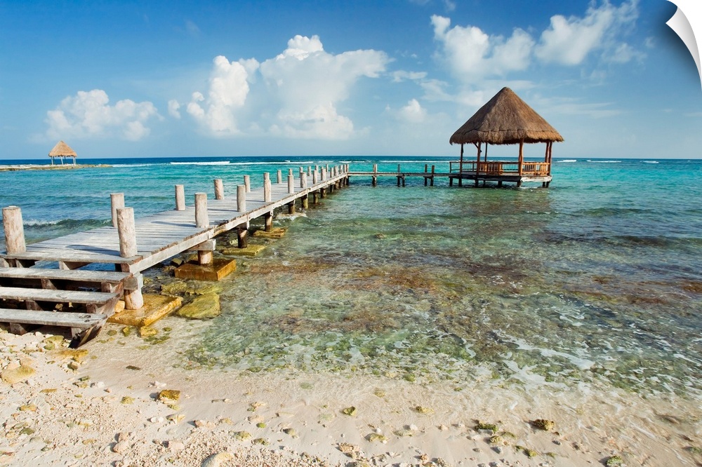 A pier stretches out into the clear ocean where there is a small hut sitting in the water.