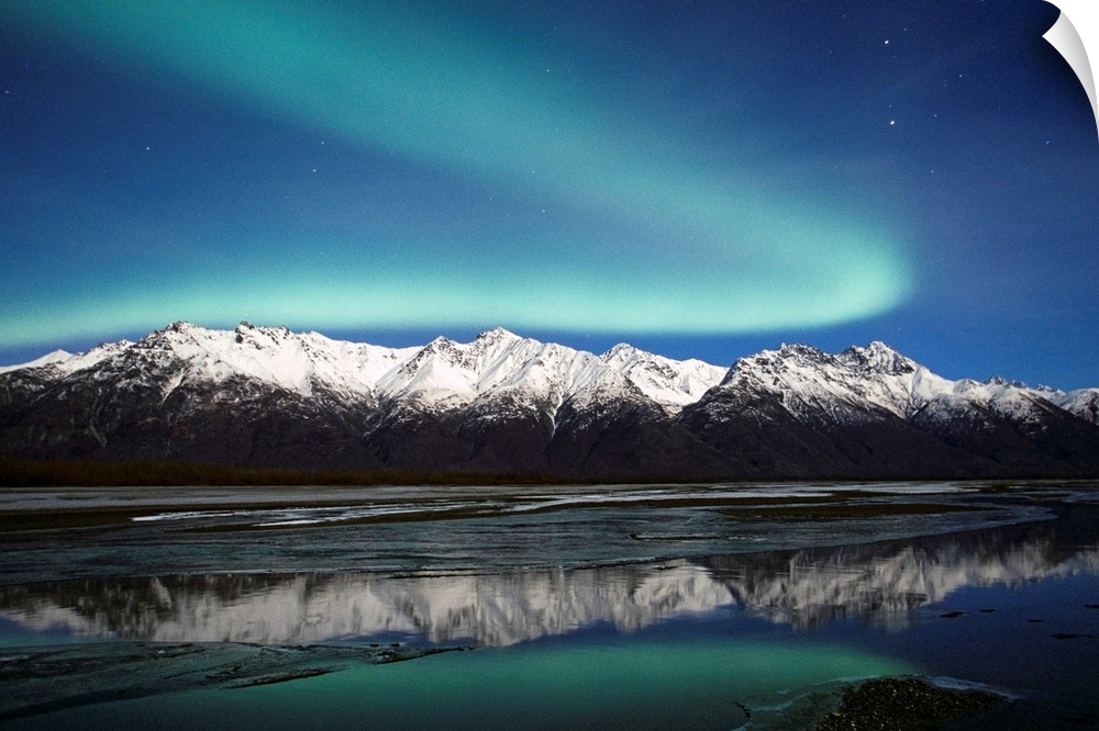 A landscape photograph of the aurora borealis and mountains reflecting in a lake filled with ice.