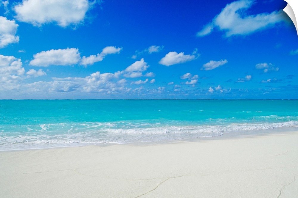 Photograph of white sandy beach and crystal clear blue waters on a calm, clear day in Hawaii.