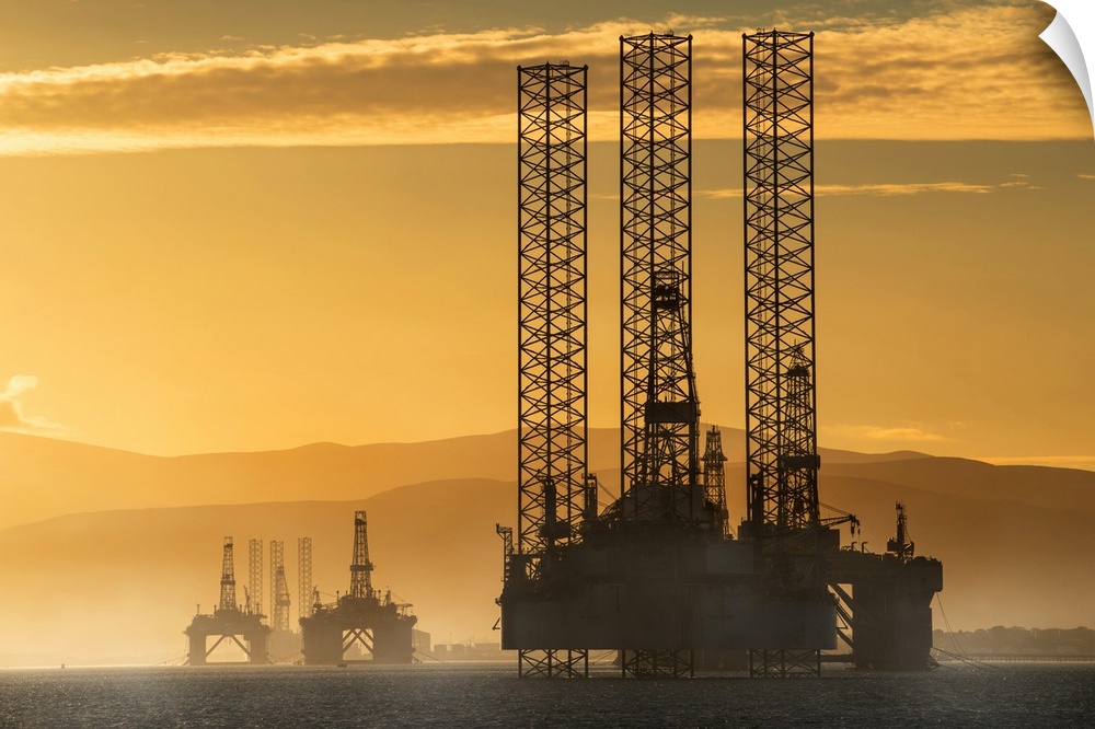 Oil drilling rigs out in the ocean with a view of the coastline and golden sunset; Cromarty, Invergordon, Scotland