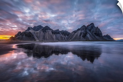 Rugged mountain peaks and a colourful sunset reflected in tranquil water, Iceland