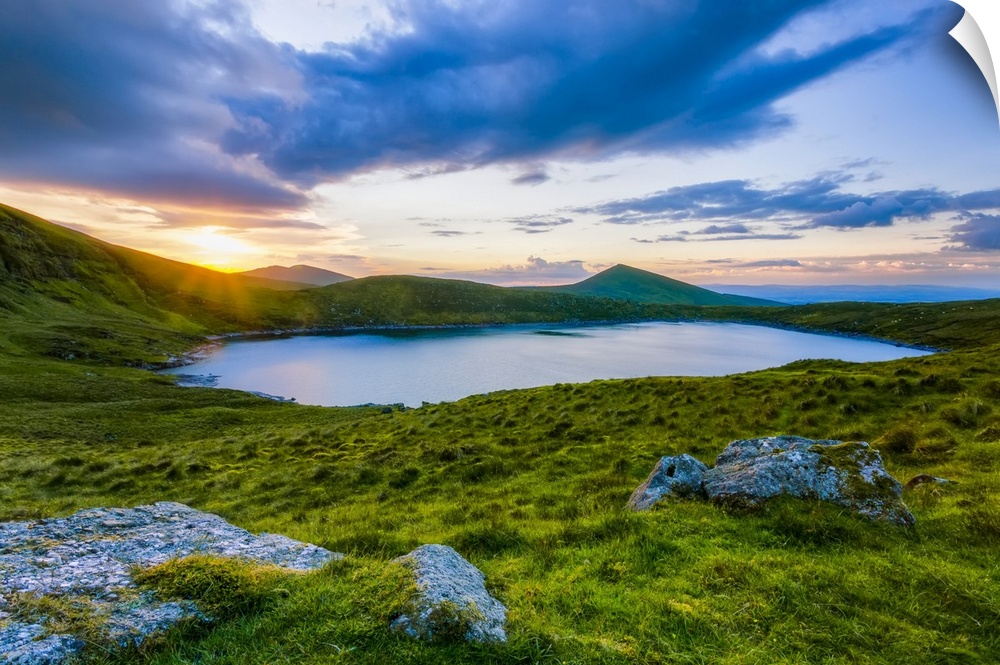 Sun setting over Lough Muskery in the Galty Mountains in summer with large boulders in the foreground, Galty Mountains; Co...