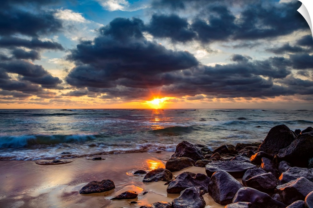 Sunrise over the Pacific Ocean from the rocks on the shore of Lydgate beach and dark clouds overhead. Kapaa, Kauai, Hawaii...