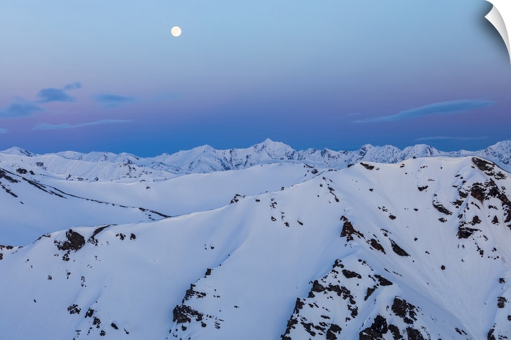 The moon rises over snowy mountain ridges after sunset in the Alaska Range; Alaska, United States of America