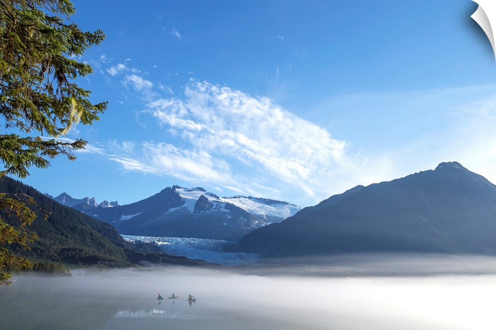 Three Kayakers paddle the shoreline of Mendenhall Lake as morning fog clears, Tongass National Forest, Juneau, Alaska.