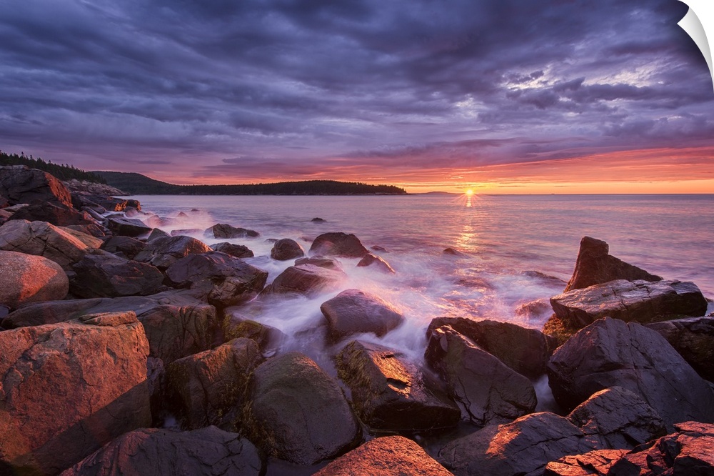 Photograph of the coast of Acadia Maine with the sun setting under purple clouds in the distance.