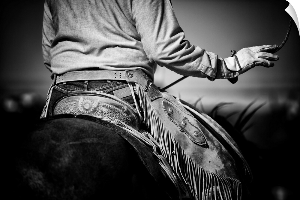 Black and white photograph of the back of a cowboy on horseback swinging his lasso.
