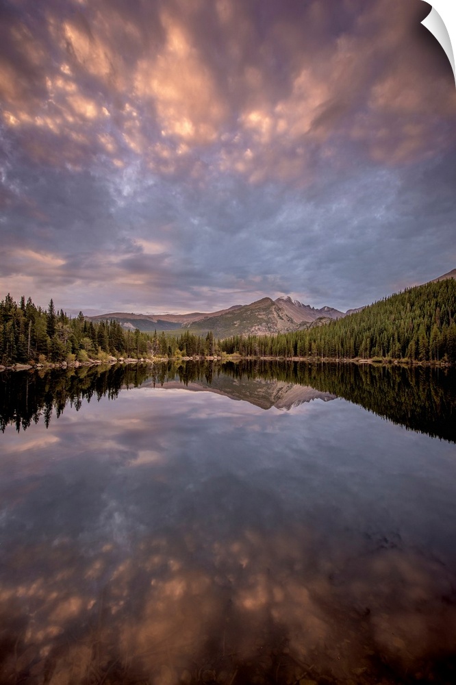 Landscape photograph of trees and mountains reflecting onto a calm lake at sunset.