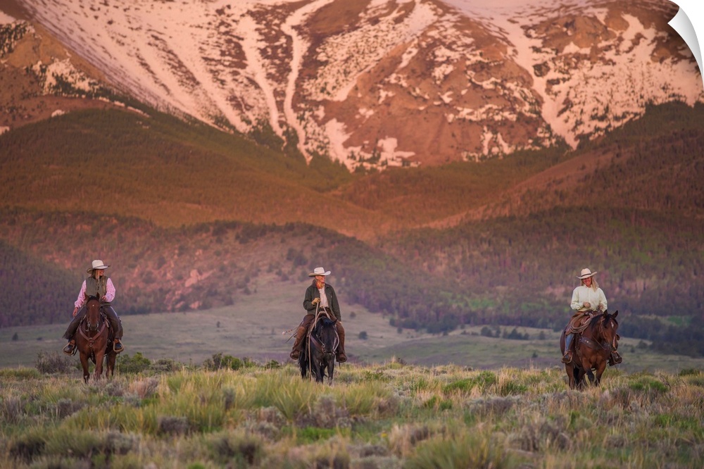 Photograph of three people on horseback in a row with snow covered mountains in the background.