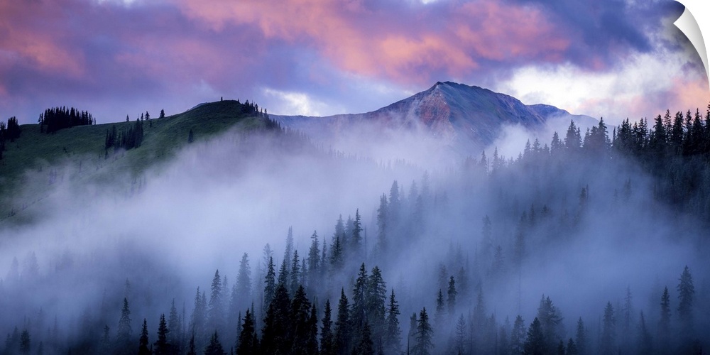 A photograph of mountain under dramatic clouds illuminated by the sunset.
