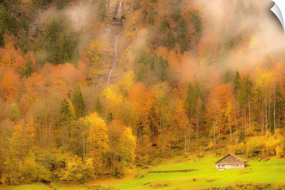 Landscape photograph of colorful Autumn trees on the side of a foggy mountain with a small cabin and waterfall.