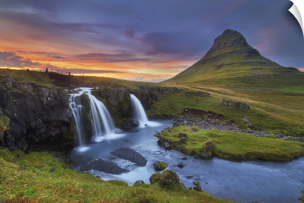 A photograph of an Icelandic landscape with waterfalls to the left and a sunset cloudscape hanging over a sloped mountain.
