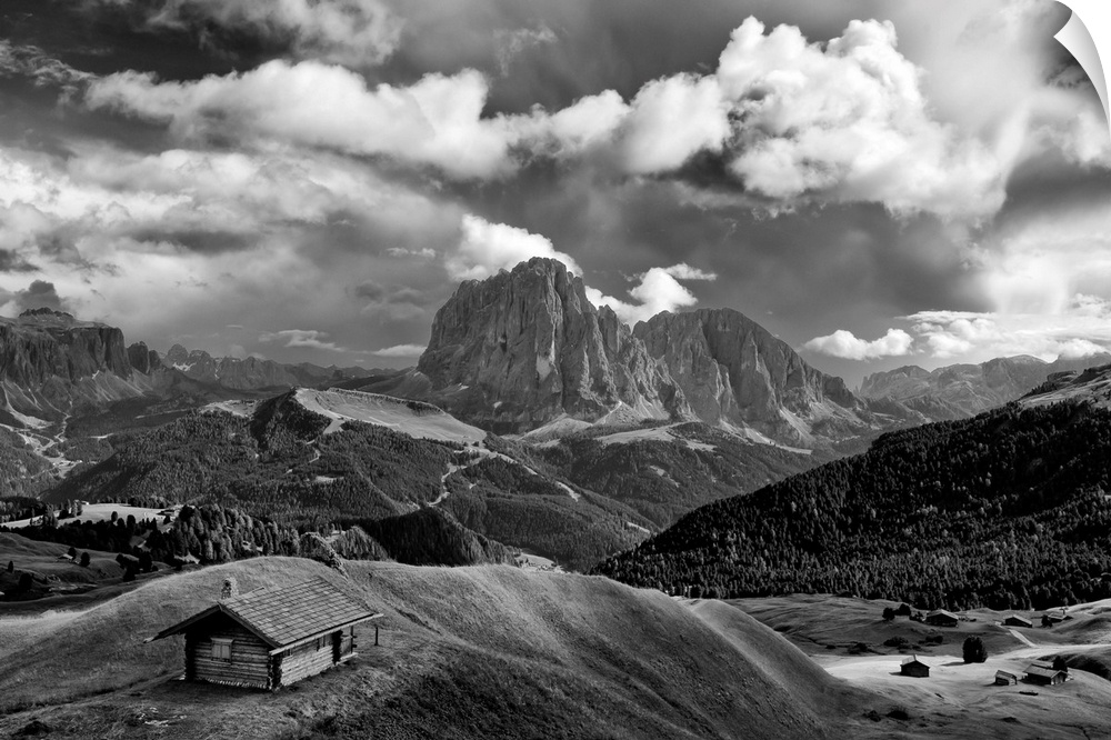 Black and white photograph of a lone cabin surrounded by rolling hills and mountains with a cloudy sky.