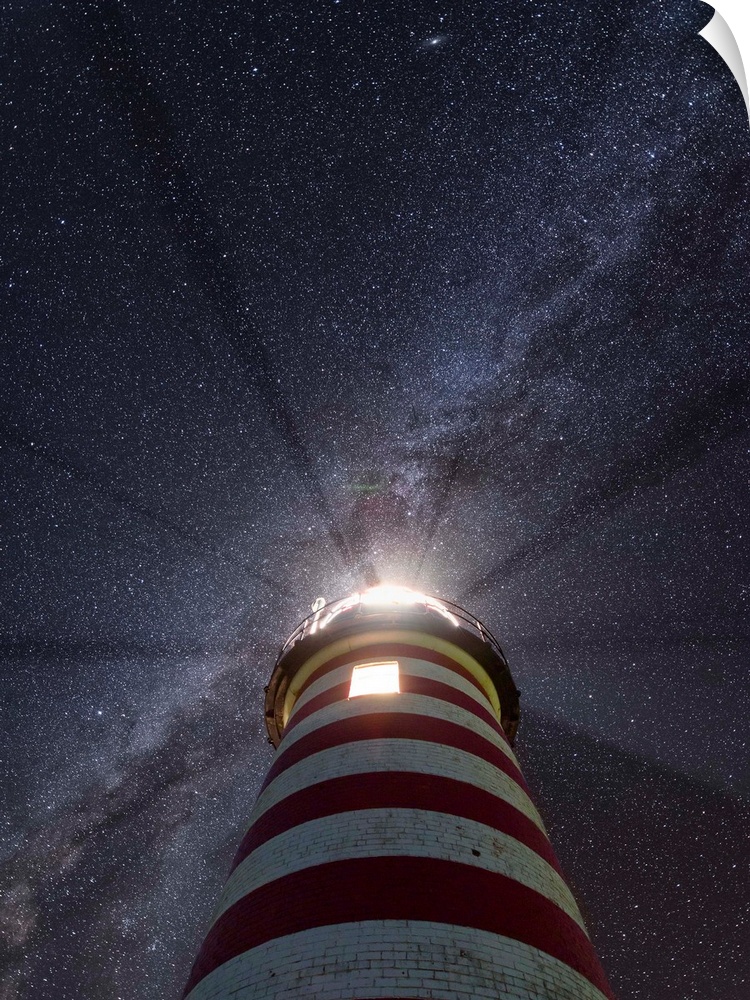 Photograph looking up at a red and white striped lighthouse to a purple and blue starry sky with the Milky Way running dia...