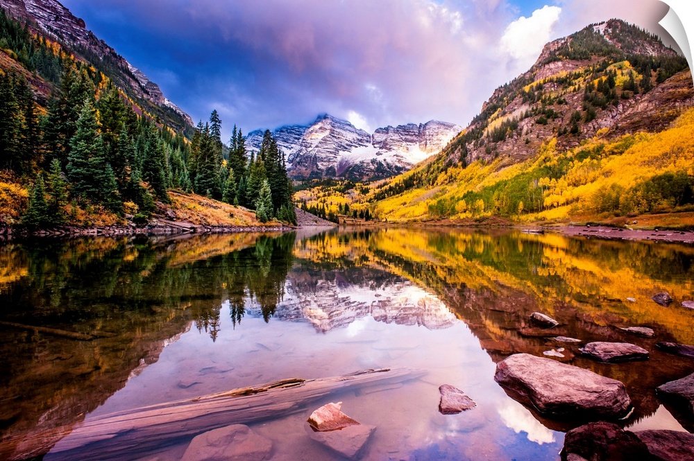 There is a warm hue to this photograph of mountainous terrain and thick foliage that reflect in still water below.