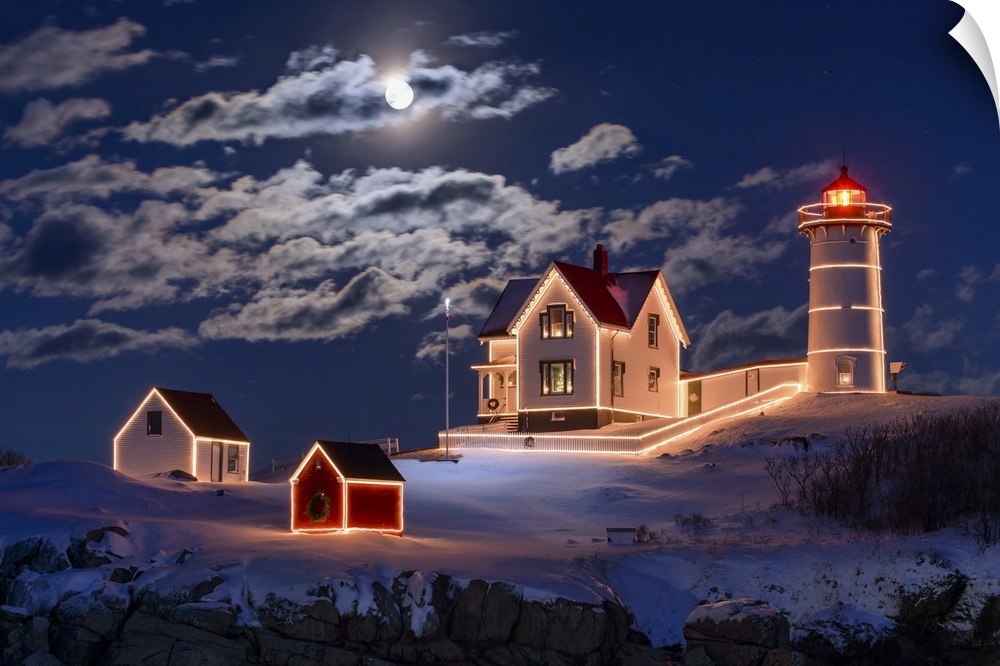 Photograph of a lighthouse and other small building outlined in lights, under a bright moon and clouds at night.