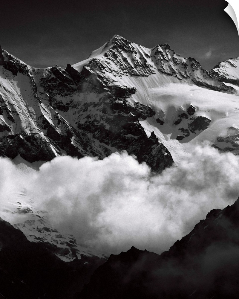 Black and white photograph of mountain peaks surrounded by rolling clouds.