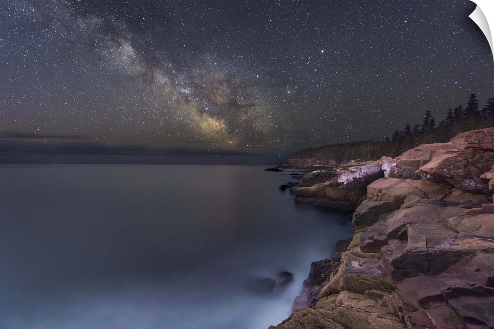 A photograph of a rocky coastline under a starry night sky.