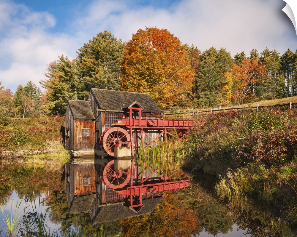 A photograph of a red water mill in the middle of a forest in autumn foliage.