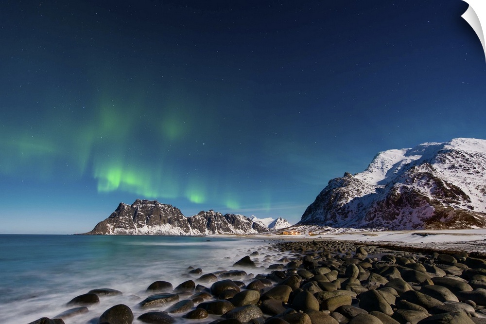 A photograph of a snow covered mountain range under a night sky with northern lights above.