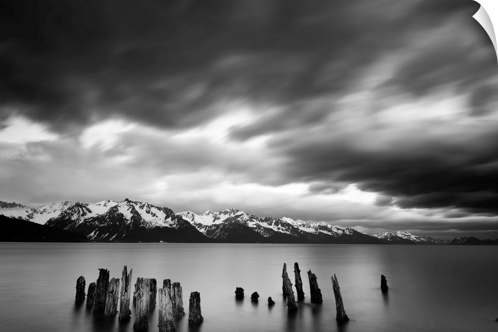 Long exposure black and white landscape photograph of a quiet lake with snow capped mountains in the distance.