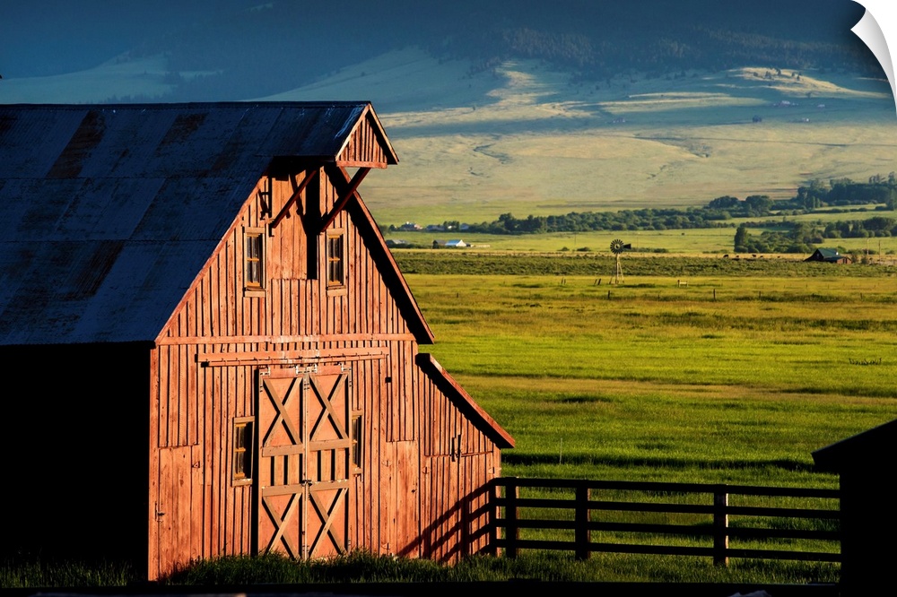 Photograph of a red barn with green farmland in the background.