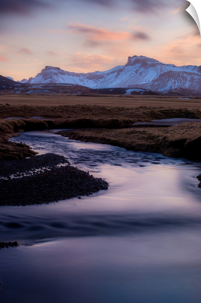 Landscape photograph of a winding river in a frozen valley with snow covered mountains in the distance.