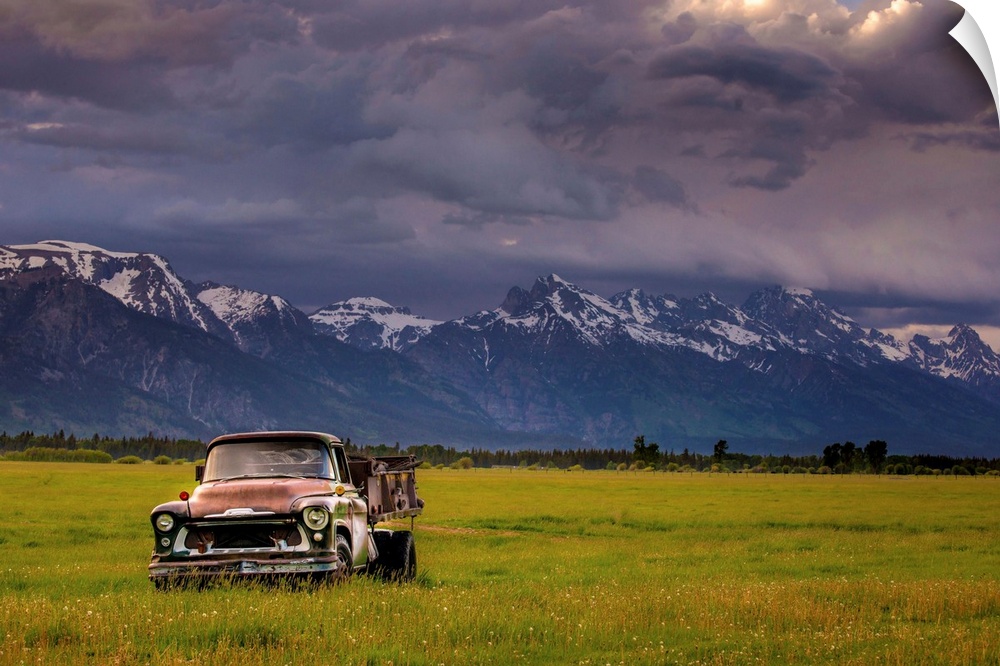 Landscape photograph of a yellow-green field with an old rusted truck and snow capped mountains in the background.