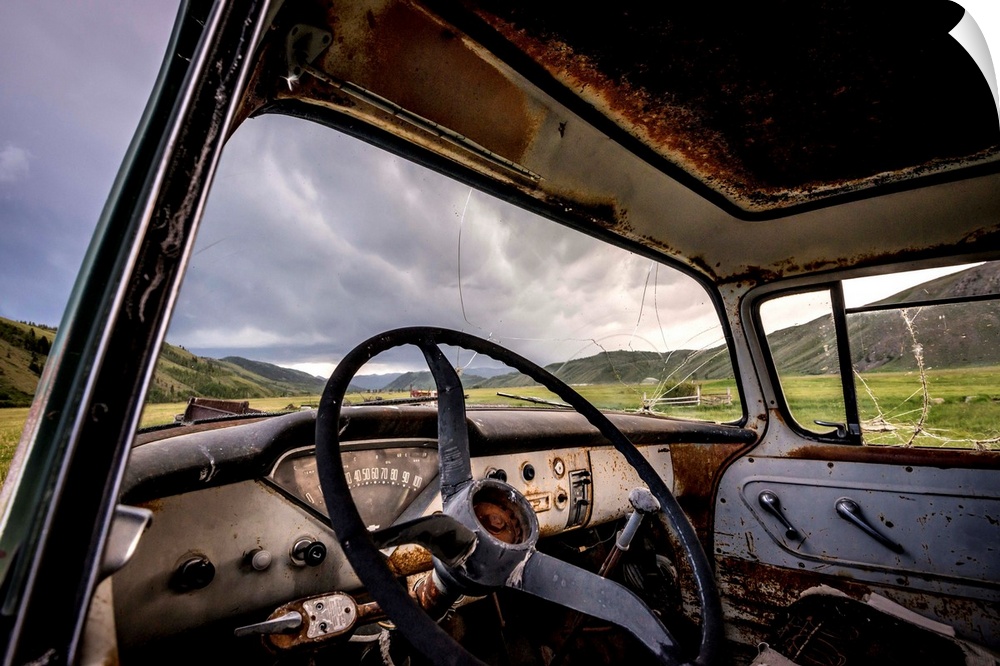 Photograph of the inside of an old abandoned car full of rust in the middle of a valley.