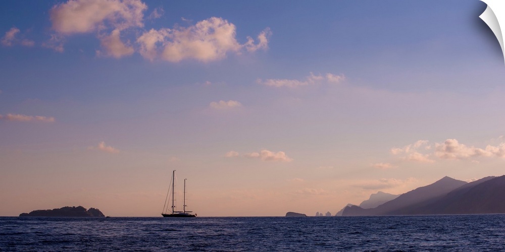 Photograph of a single sailboat in the middle of the ocean with silhouettes of mountains in the distance.